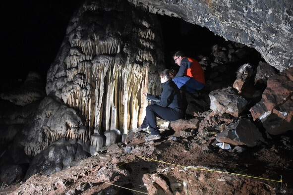 Two people sitting in a cade facing a stalagmite