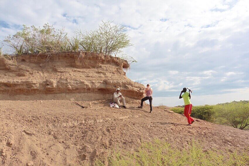 Three researchers sitting by rock outcrop